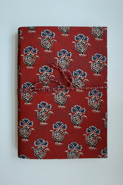A handmade journal with a red cover featuring a blue and cream block print pattern, wrapped with a red and white twine tie.