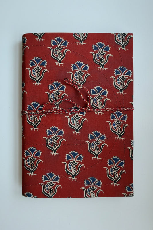 A handmade journal with a red cover featuring a blue and cream block print pattern, wrapped with a red and white twine tie.